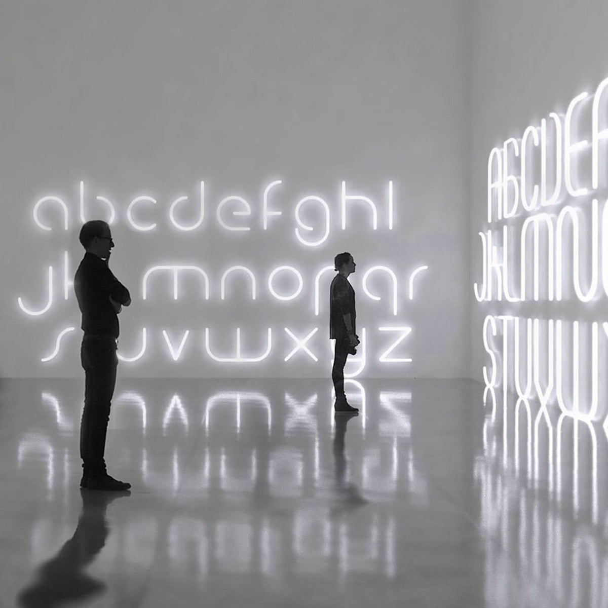 Deux personnes devant une grande installation murale lumineuse en lettres.