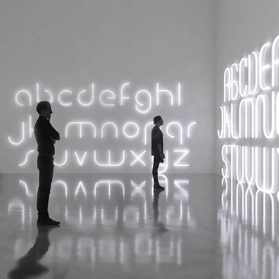 Deux personnes devant une grande installation murale lumineuse en lettres.