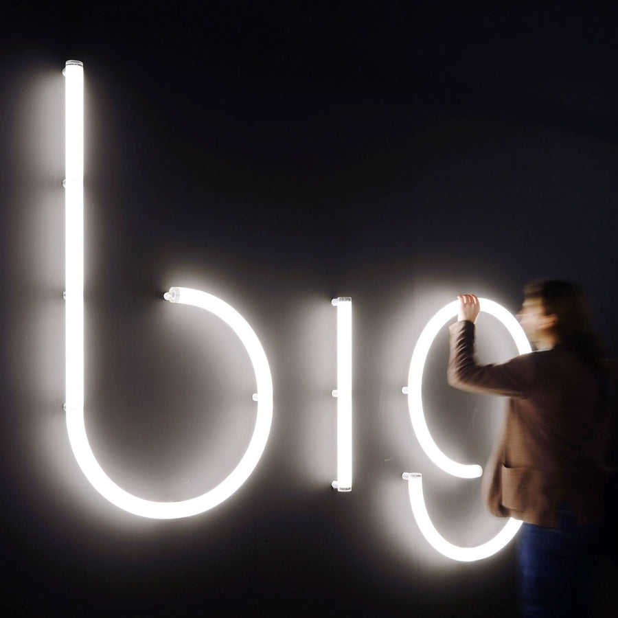 Une personne installe une grande lettre lumineuse blanche sur un mur noir.