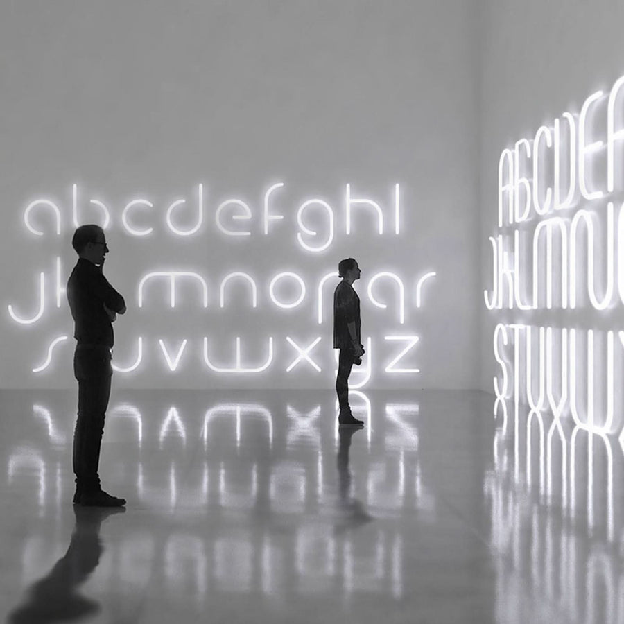 Deux silhouettes observent de grandes lettres lumineuses blanches sur les murs d'une galerie.