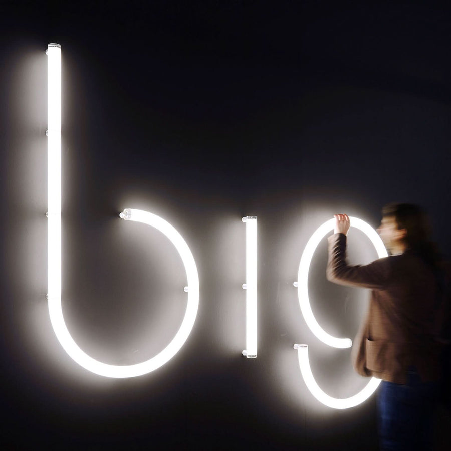 Personne ajustant de grandes lettres lumineuses blanches fixées sur un mur sombre.