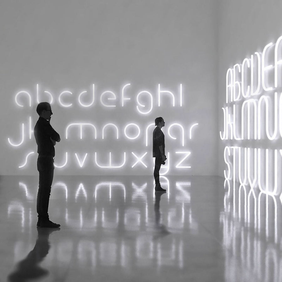 Deux personnes contemplent des lettres lumineuses géantes dans une galerie sombre et réfléchissante.
