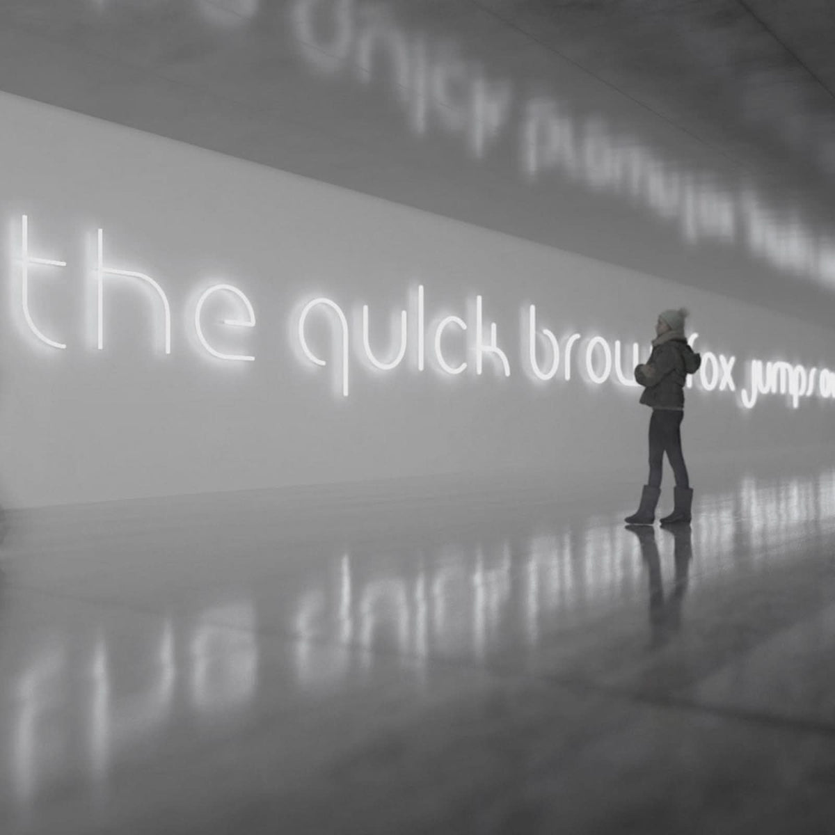 Femme devant la phrase lumineuse the quick brown fox sur un mur clair.