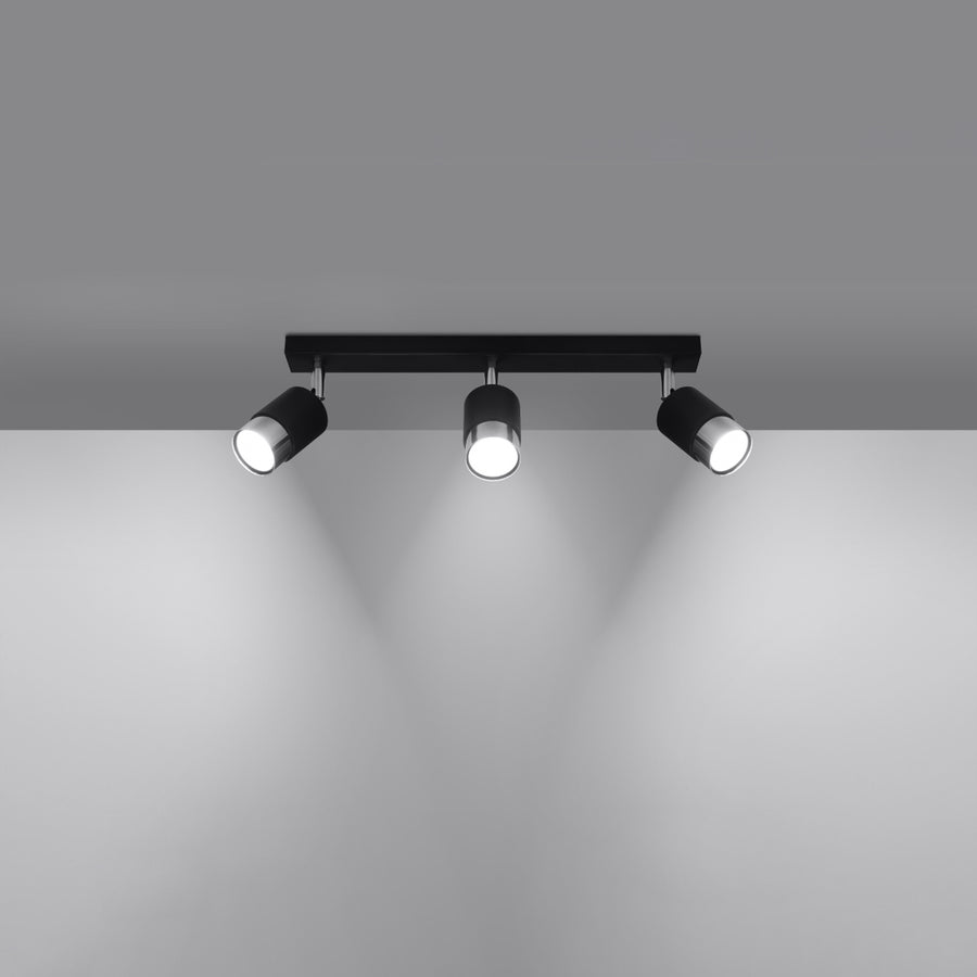 Plafonnier allumé dans une pièce sombre, trois faisceaux lumineux orientables vers le bas.