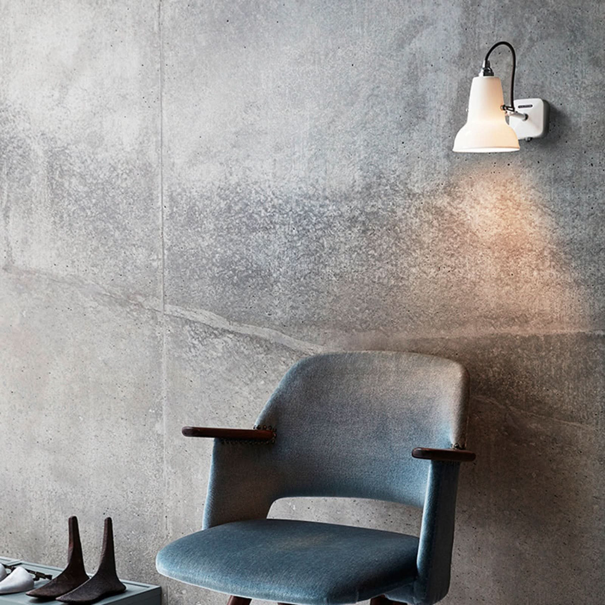 Applique murale fixée sur un mur en béton brut au-dessus d’un fauteuil bleu.