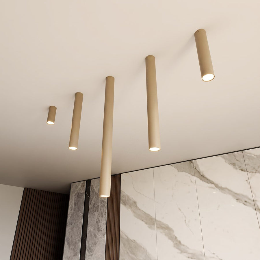 Cinq tubes beige de longueurs différentes au plafond, devant un mur de marbre veiné.