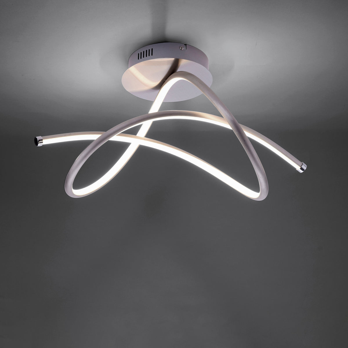 Plafonnier allumé dans une pièce sombre, soulignant les courbes des tubes LED.