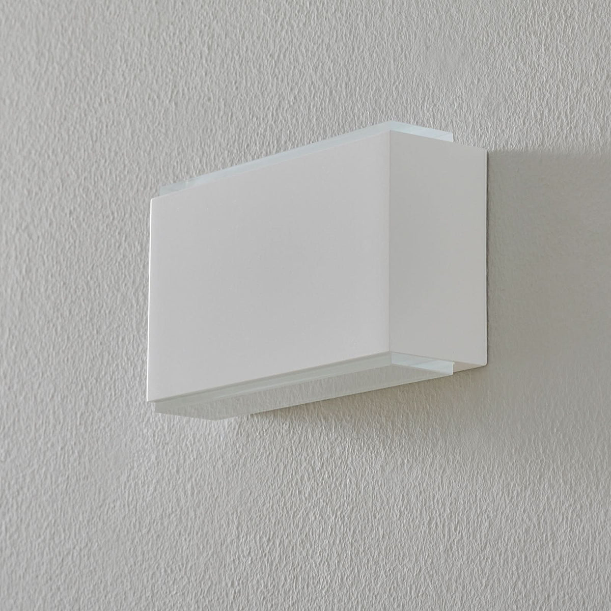 Vue de face de l’applique blanche éteinte, fixée au mur.