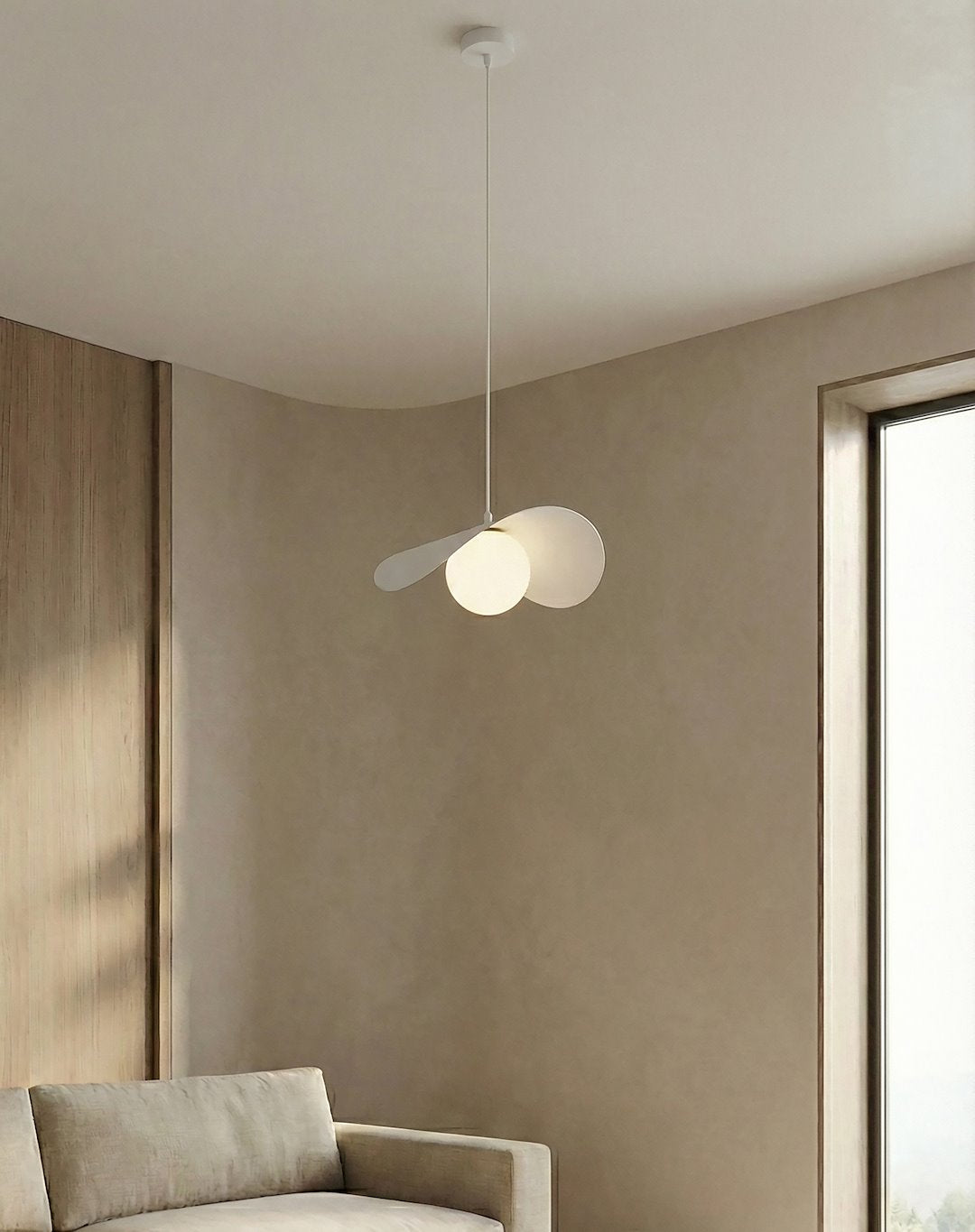 Mise en ambiance au-dessus d'un canapé beige, suspension blanche allumée près d'une fenêtre.
