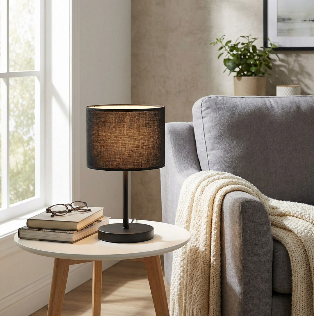 Scène de vie avec lampe sur table d'appoint, fauteuil gris et plaid tricoté.