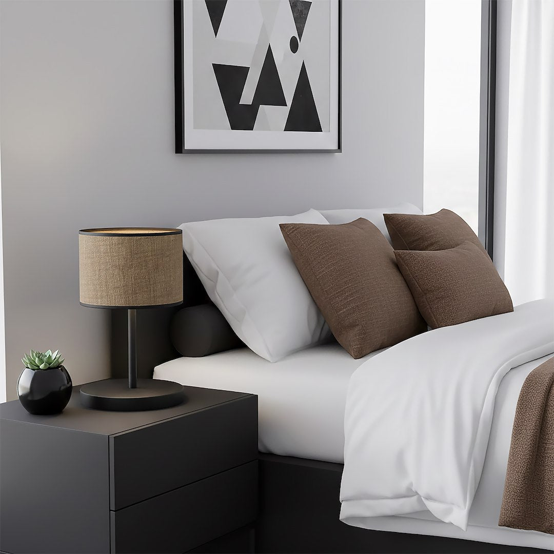 Lampe allumée sur chevet noir, lit blanc et coussins marron en chambre