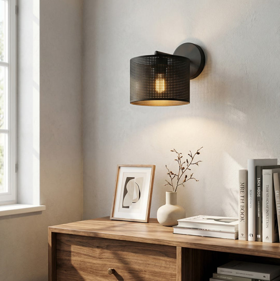 Luminaire allumé sur mur blanc, halo doré traversant la perforation au-dessus d'ouvrages