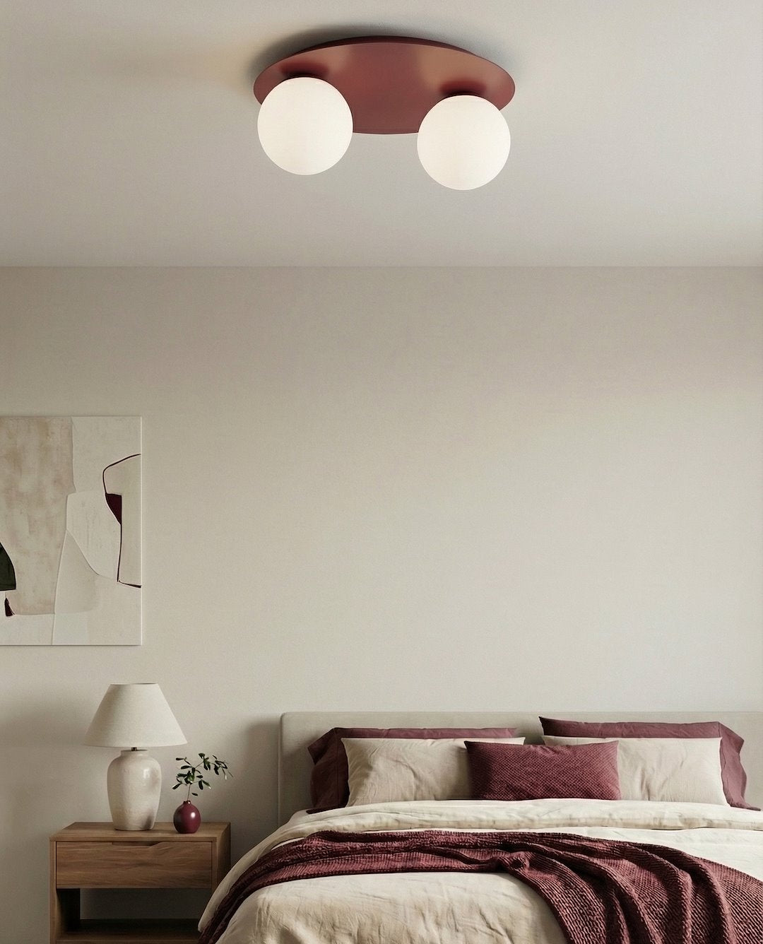 Mise en ambiance dans une chambre avec le plafonnier bordeaux au plafond, lit et coussins assortis.