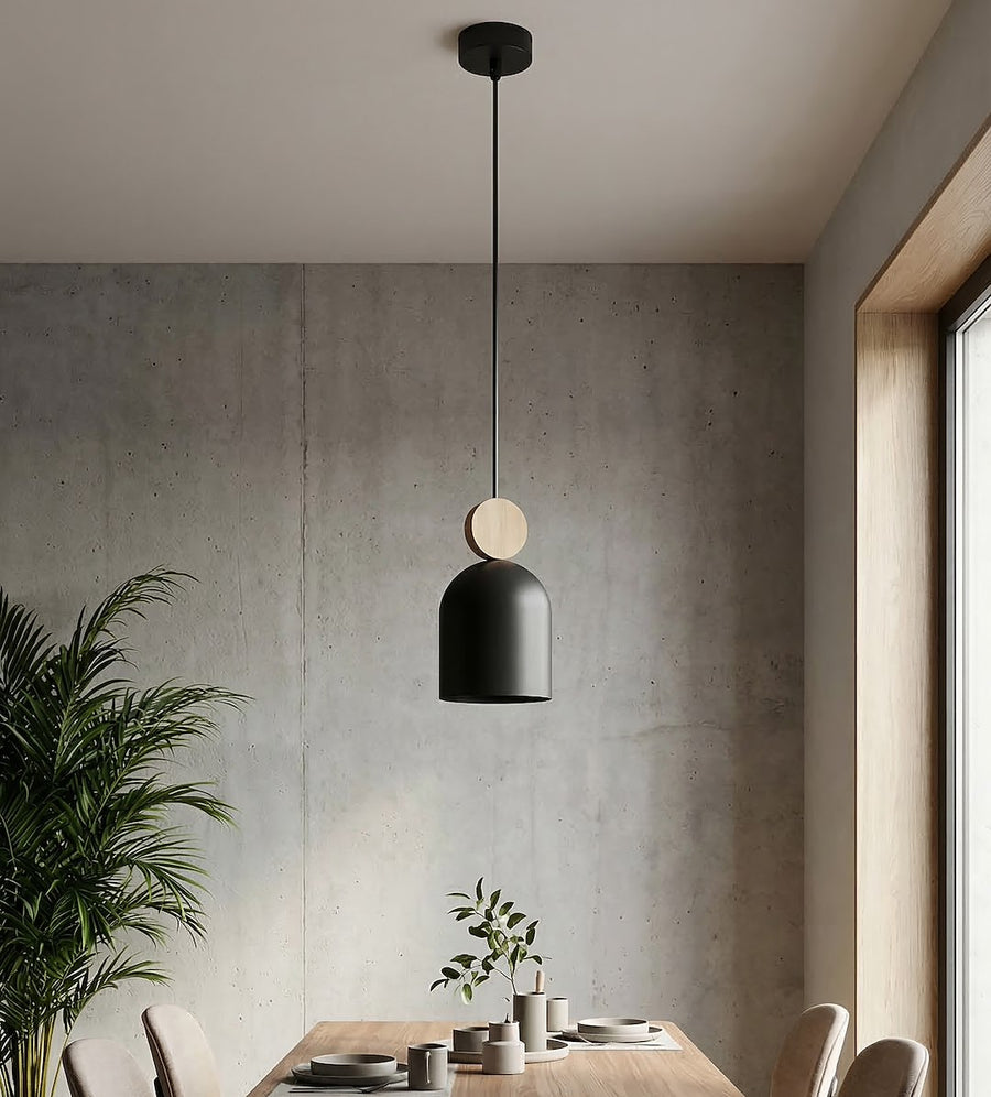 Ambiance béton avec suspension noire au-dessus d'une table et d'une plante.