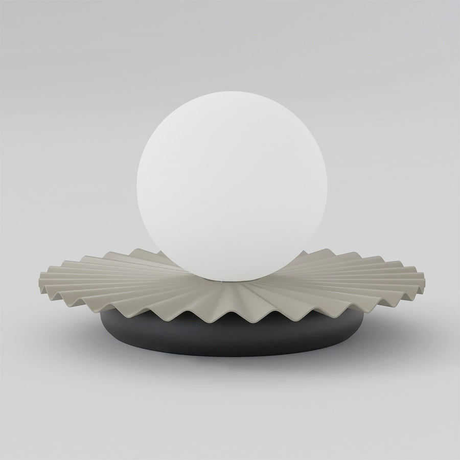 Lampe à poser de face, globe blanc en verre sur base plissée beige et socle noir.