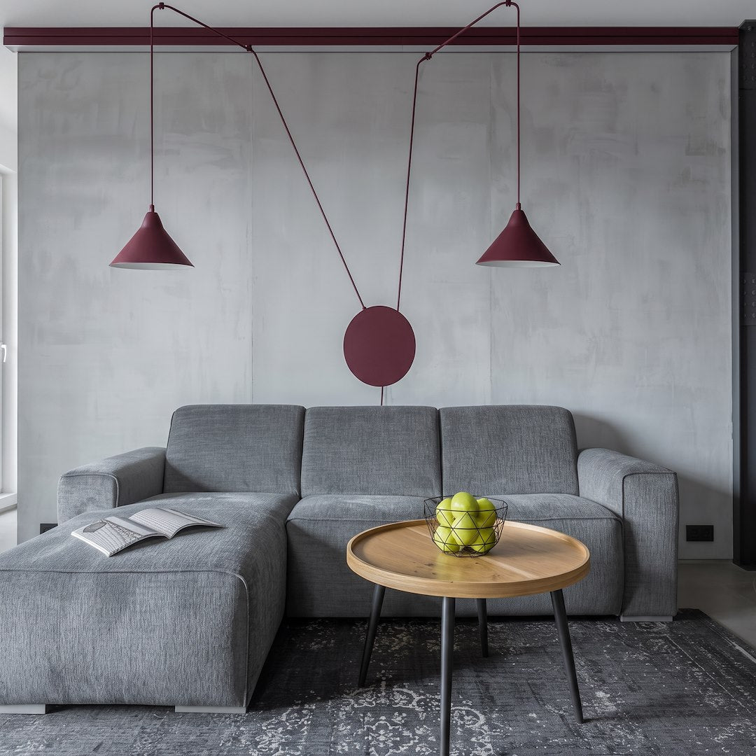 Ambiance salon avec canapé gris, les deux suspensions bordeaux suspendues devant un mur béton.