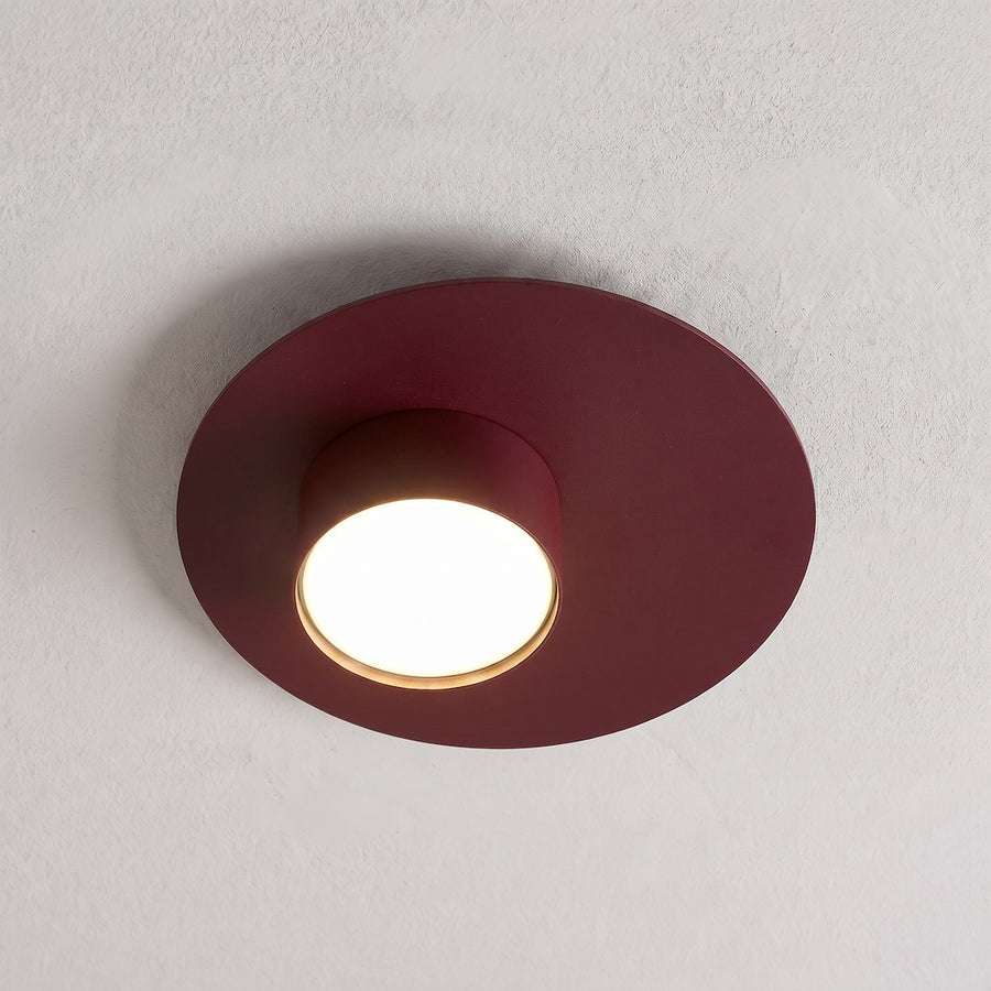 Plafonnier bordeaux allumé au plafond, halo lumineux chaud sur mur blanc