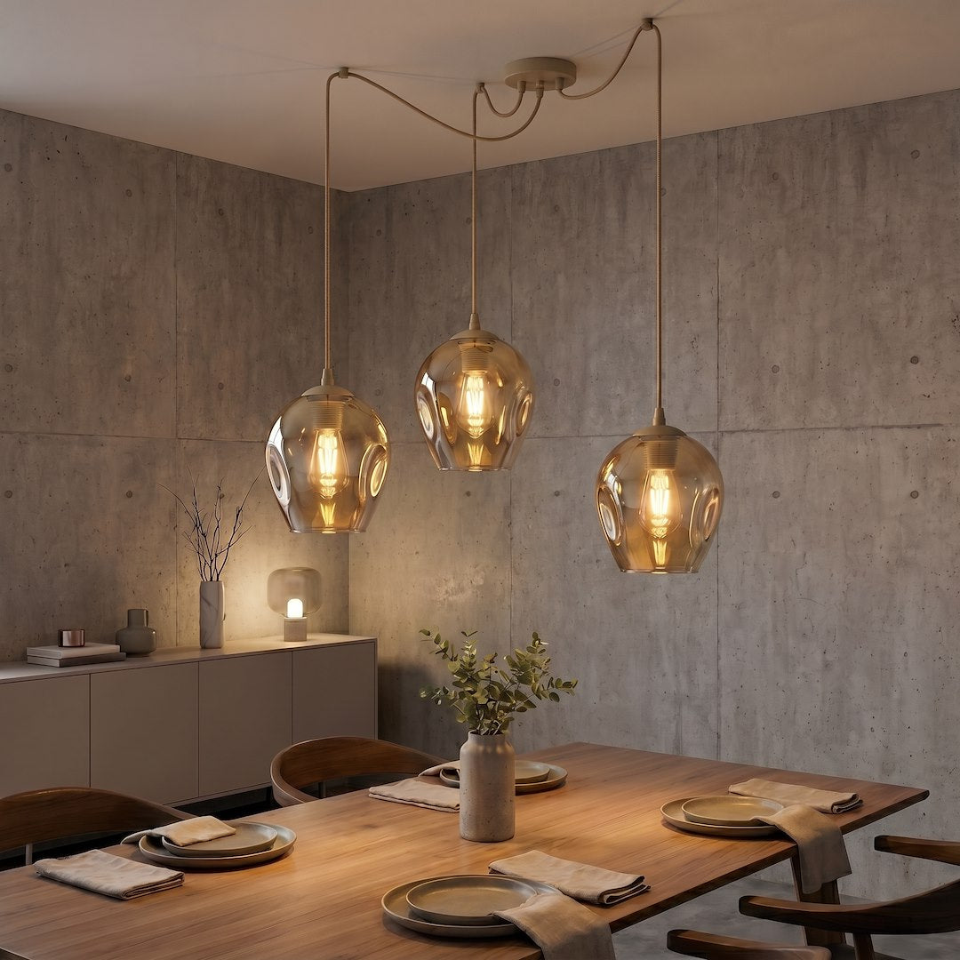 Mise en ambiance salle à manger béton, trois suspensions allumées au-dessus d'une table en bois