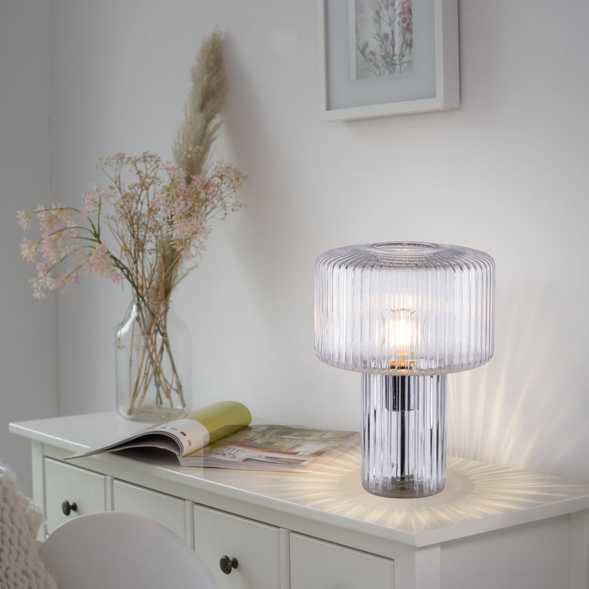 Mise en ambiance dans une chambre blanche, lampe posée sur une commode.
