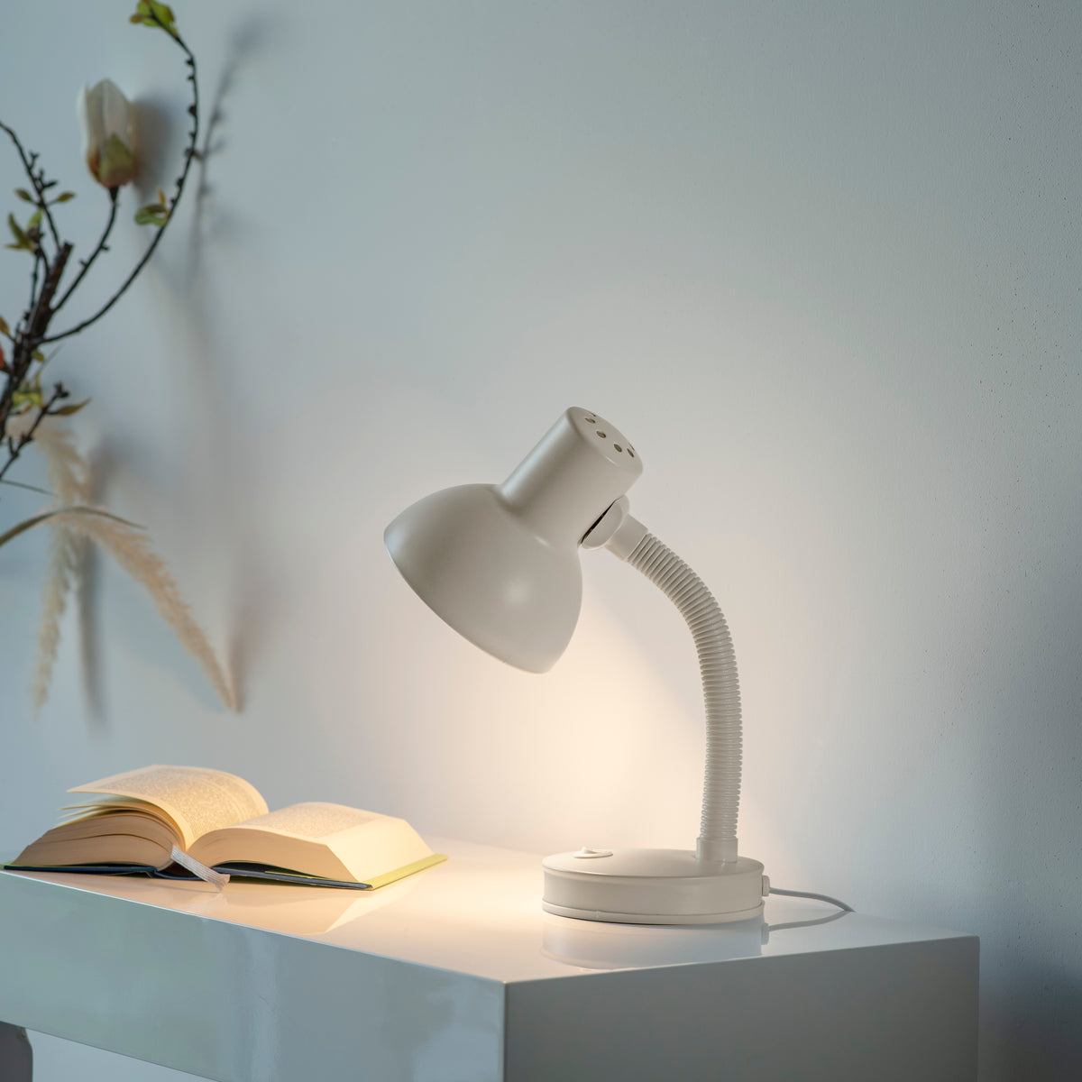 Lampe posée sur une table blanche près d'un livre ouvert, dans une ambiance chaleureuse.