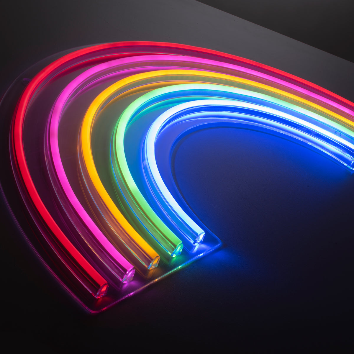Détail des tubes néon souples et socle transparent, éclairage multicolore sur fond sombre.