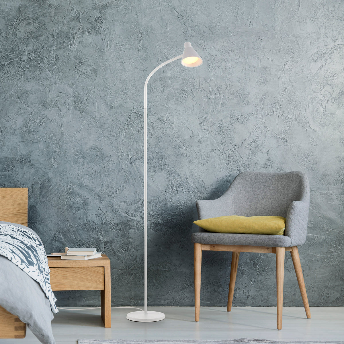 Mise en ambiance chambre : lampadaire devant mur gris texturé, fauteuil et table de chevet