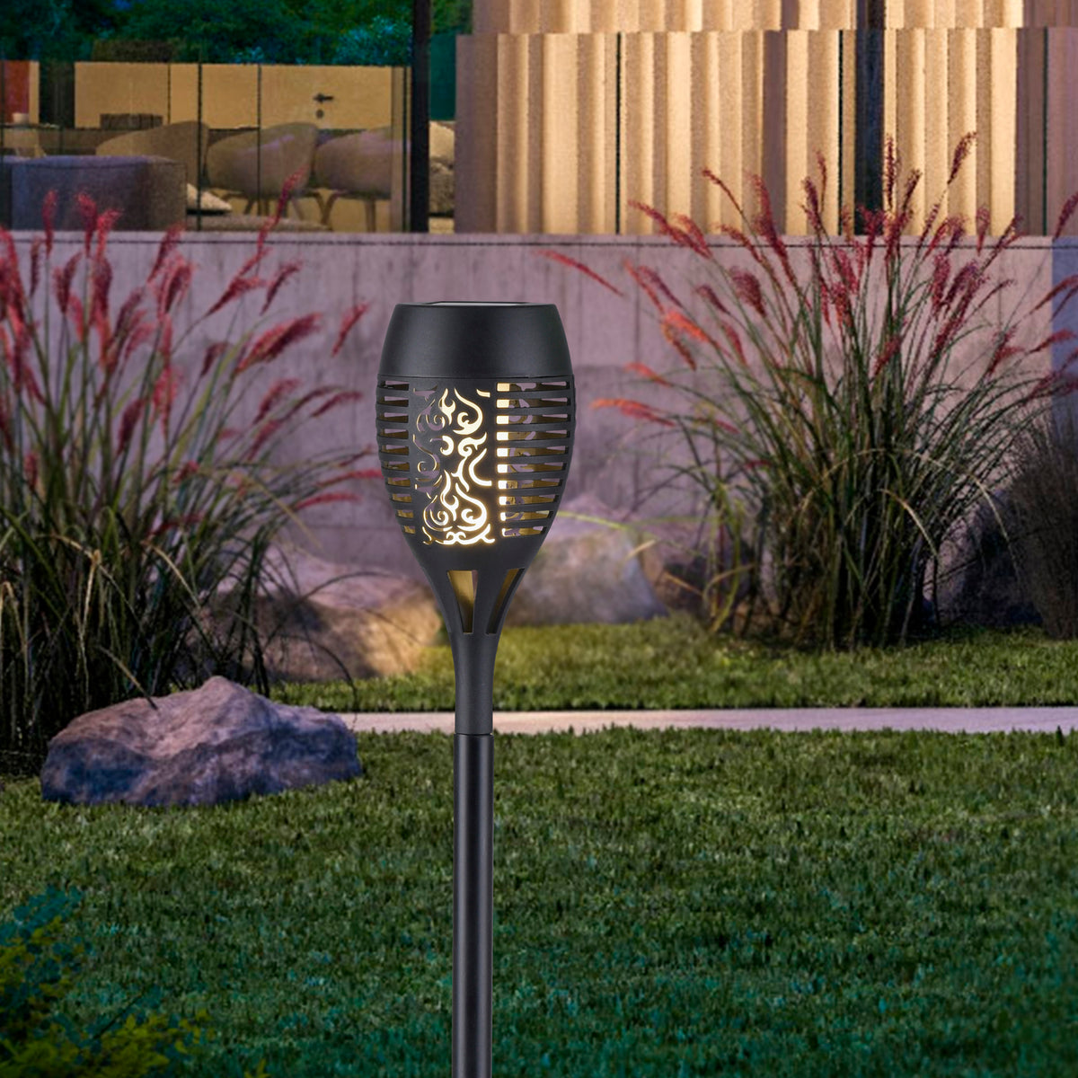 Piquet lumineux allumé dans un jardin, effet flamme doré éclairant la pelouse.