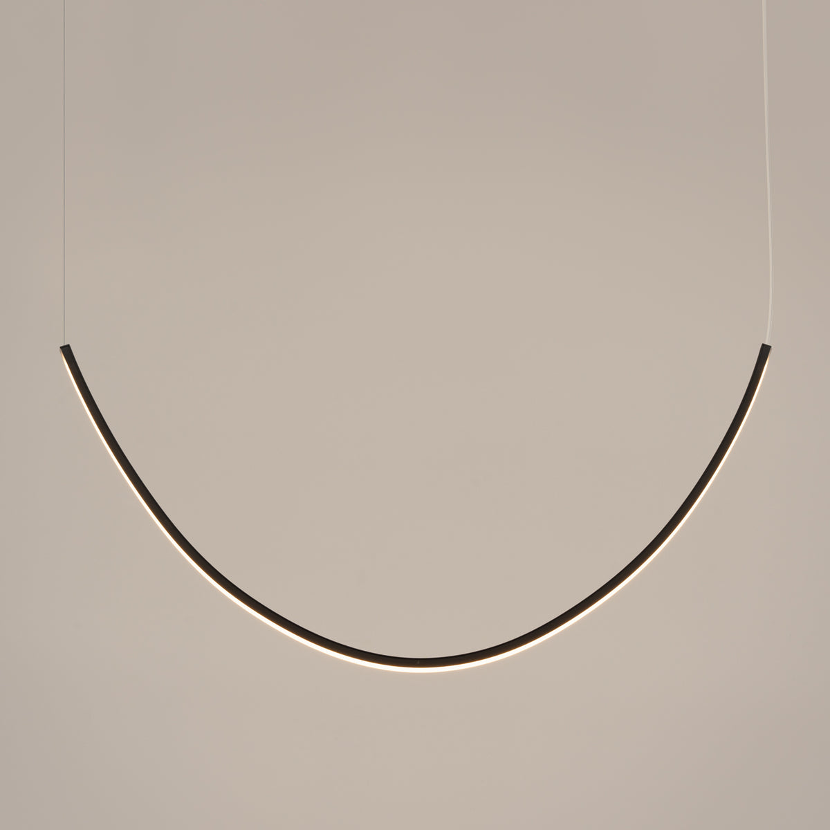 Luminaire en arche éclairé de face sur mur beige, câbles fins invisibles