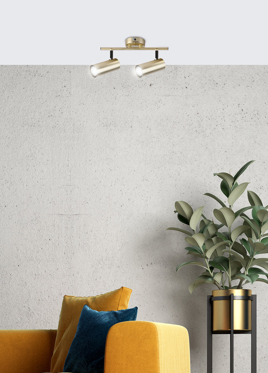 Vue en situation sur mur béton, luminaire laiton éclairant canapé jaune et plante verte.