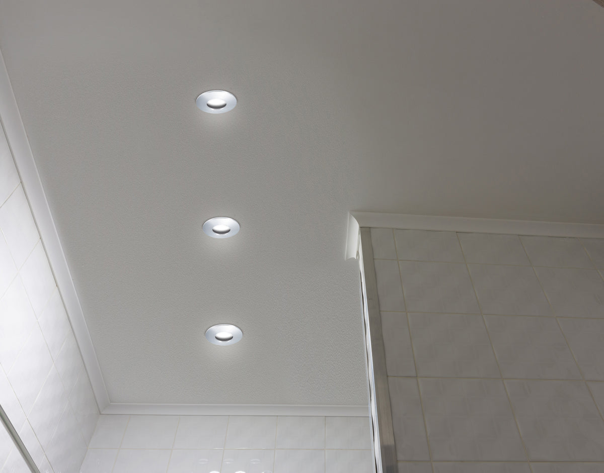 Trois spots encastrés allumés alignés au plafond blanc d'une salle de bain carrelée
