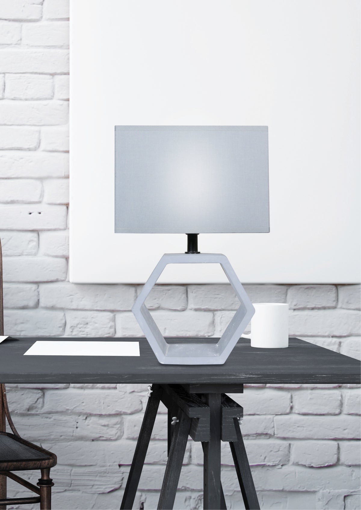 Mise en ambiance, lampe allumée posée sur table noire devant mur de briques
