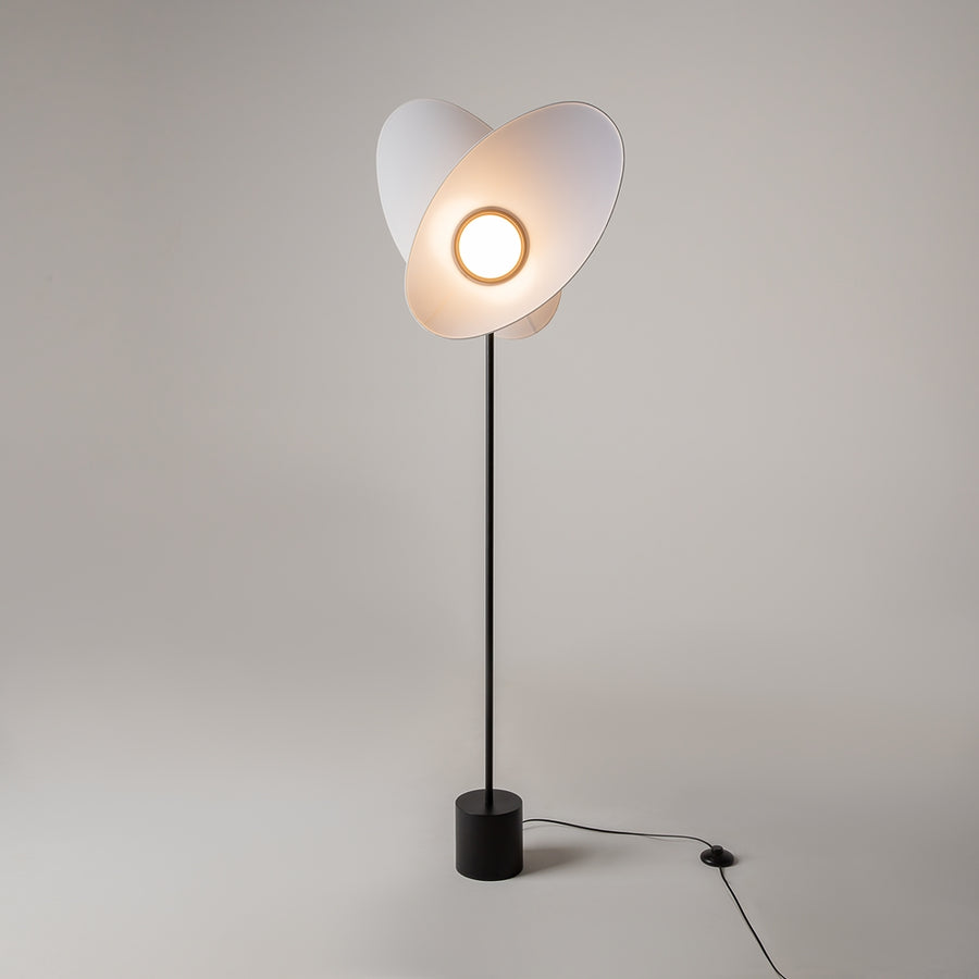 Lampadaire allumé dans une pièce claire, halo chaud entre les pétales.