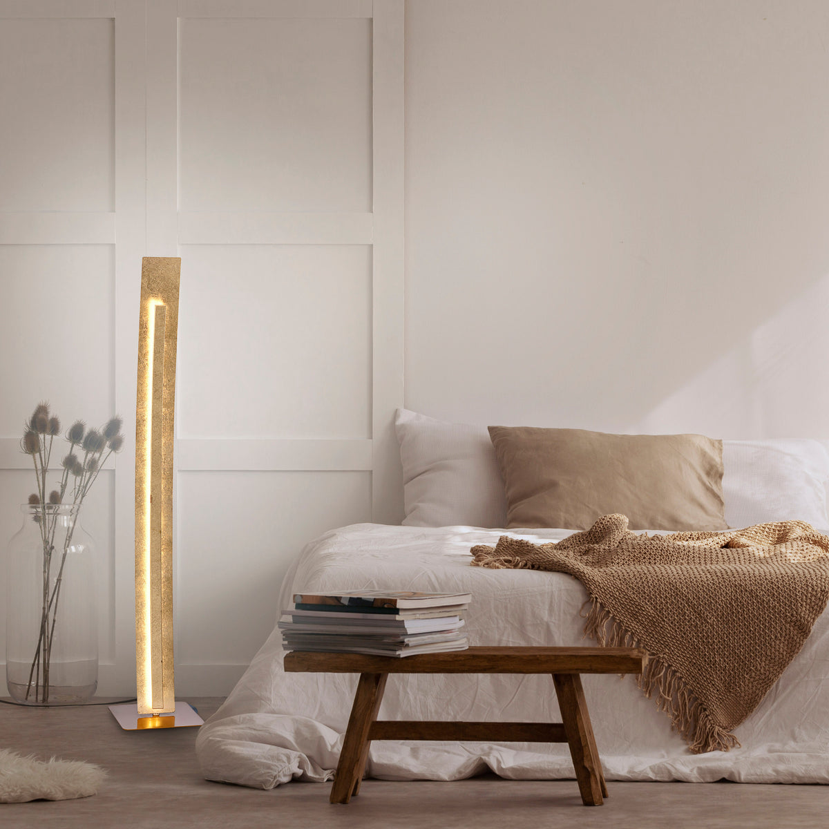 Mise en ambiance d'une chambre avec le lampadaire doré allumé près du lit.