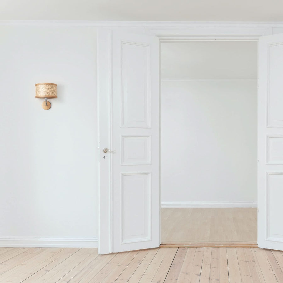 Applique murale en bois et fibres claires fixée sur un mur blanc, près d'une porte ouverte.