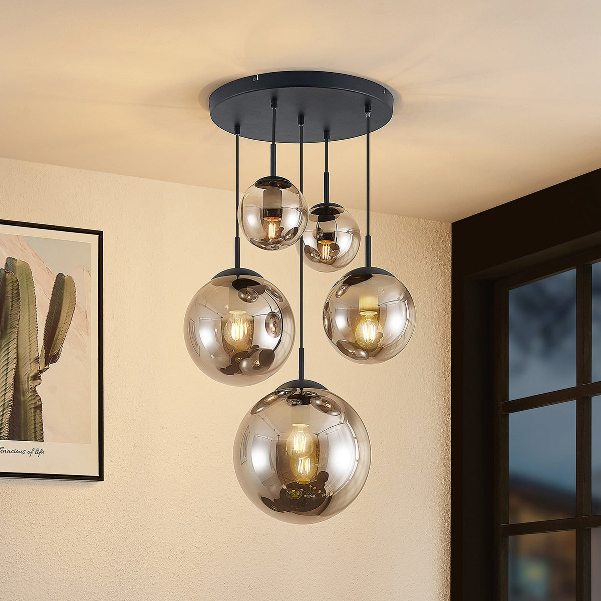 Suspension à cinq globes en verre fumé allumés, installée dans un salon.