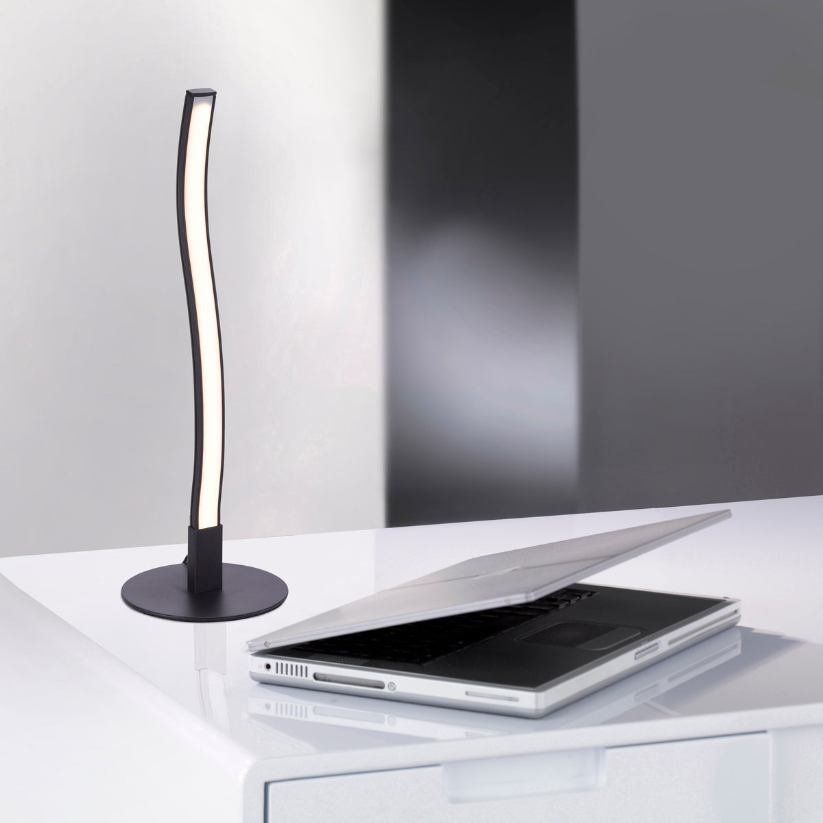 Mise en ambiance bureau, lampe posée près d'un ordinateur portable ouvert sur table blanche.
