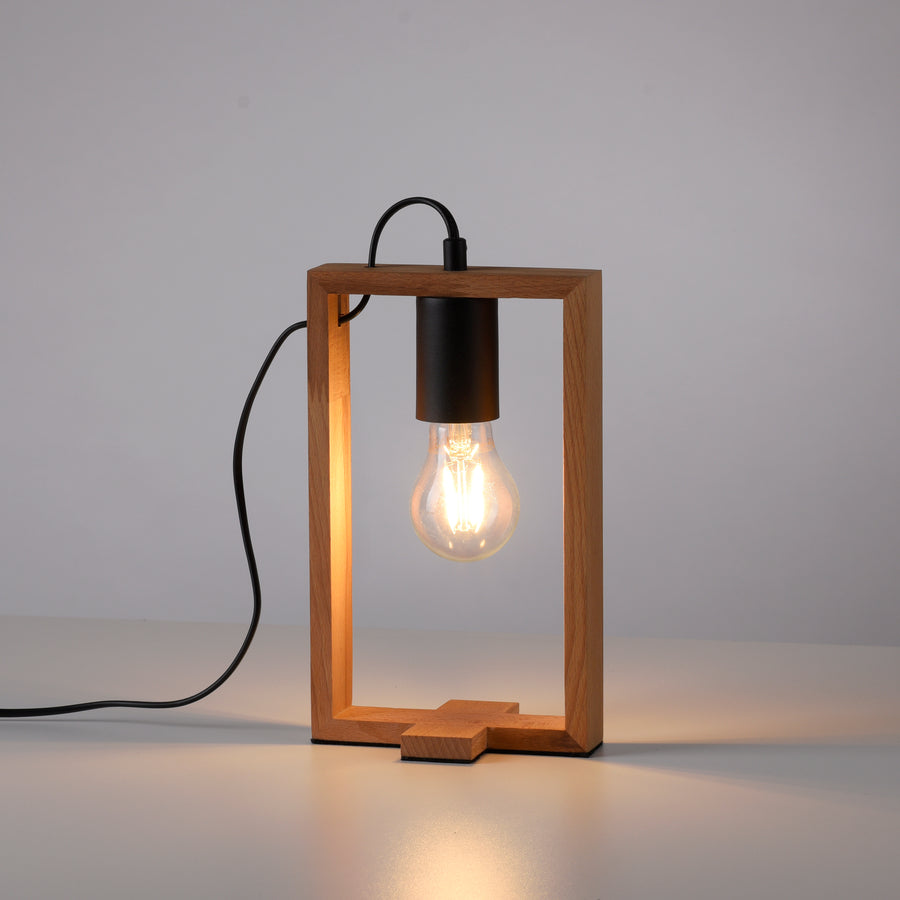Lampe en bois allumée posée sur surface blanche, ampoule Edison brillante et câble noir.