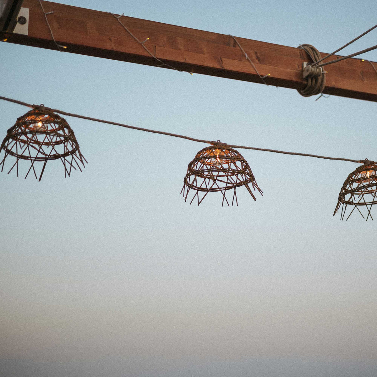 Vue en contre-plongée de trois cloches tressées sous une poutre en bois, ciel pâle.