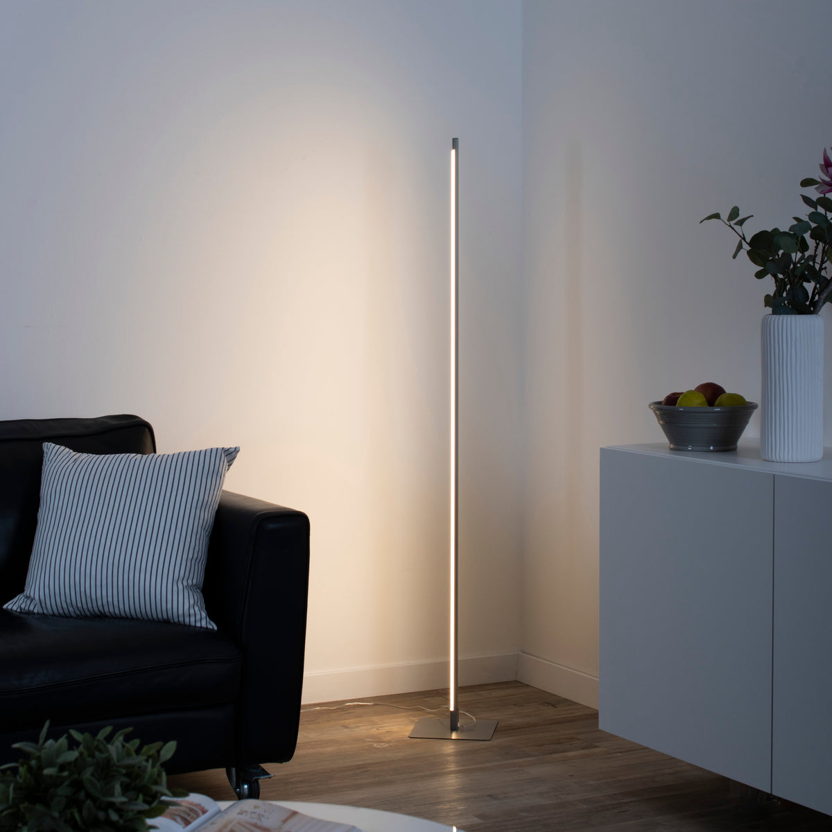 Mise en ambiance salon avec lampadaire allumé près d'un canapé et d'un meuble.