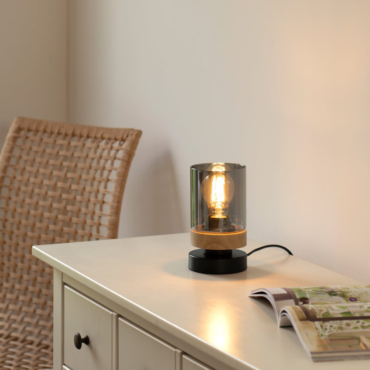 Mise en ambiance sur une commode blanche, lampe allumée près d'une chaise en cannage.