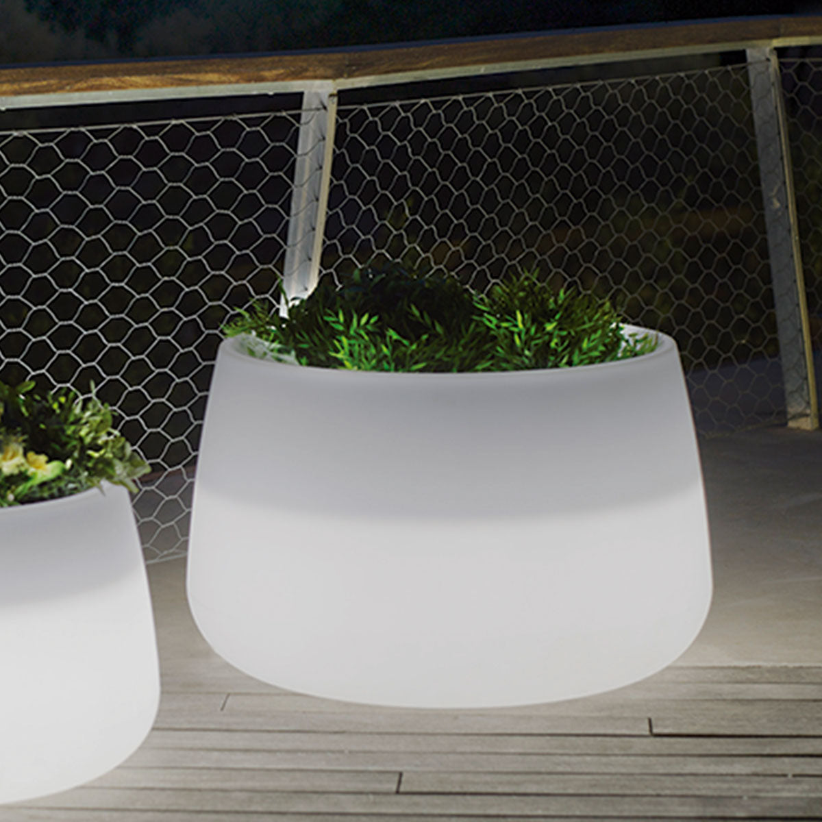 Gros plan sur la grande jardinière blanche allumée la nuit sur le platelage