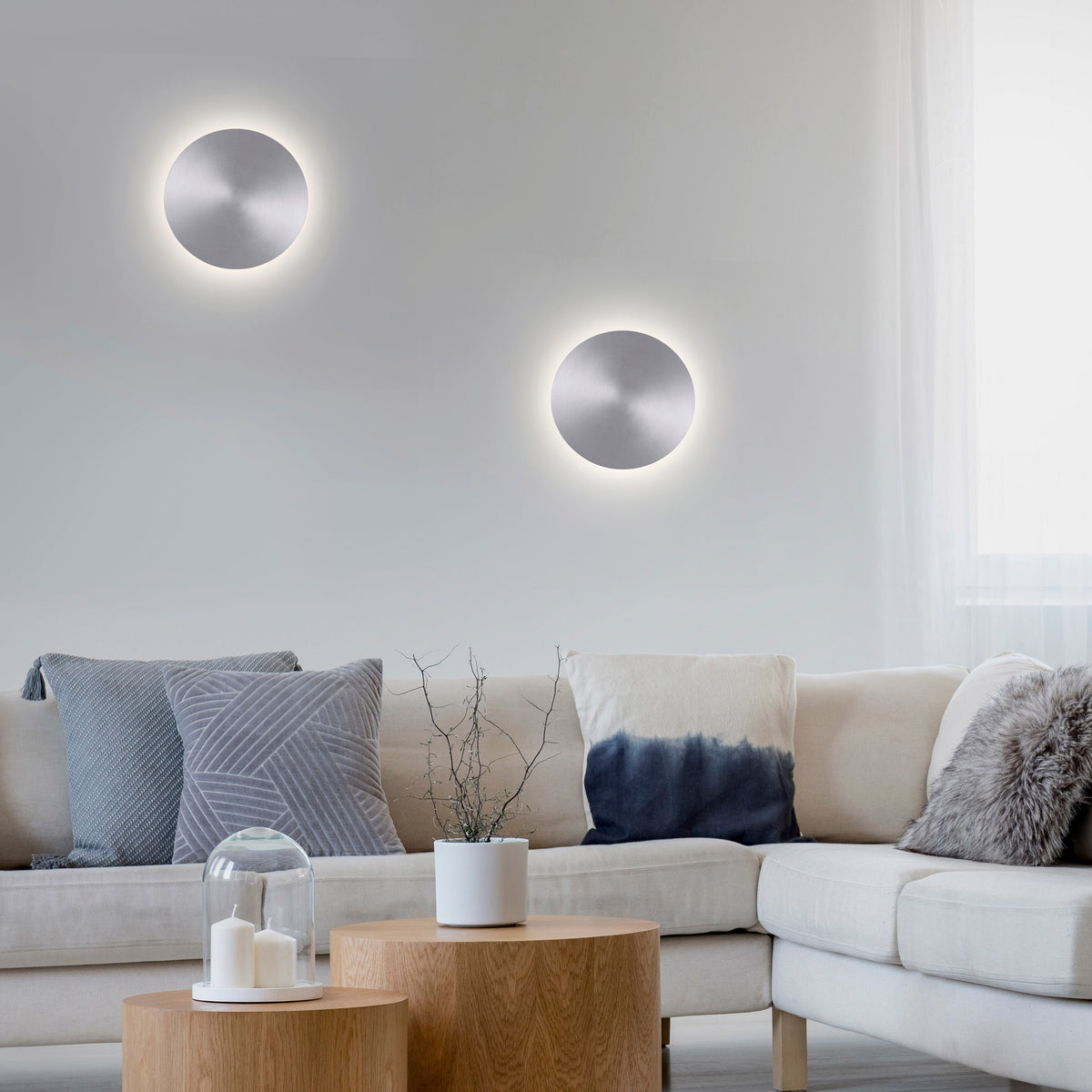 Mise en ambiance avec deux appliques murales rondes allumées au-dessus d'un canapé beige.