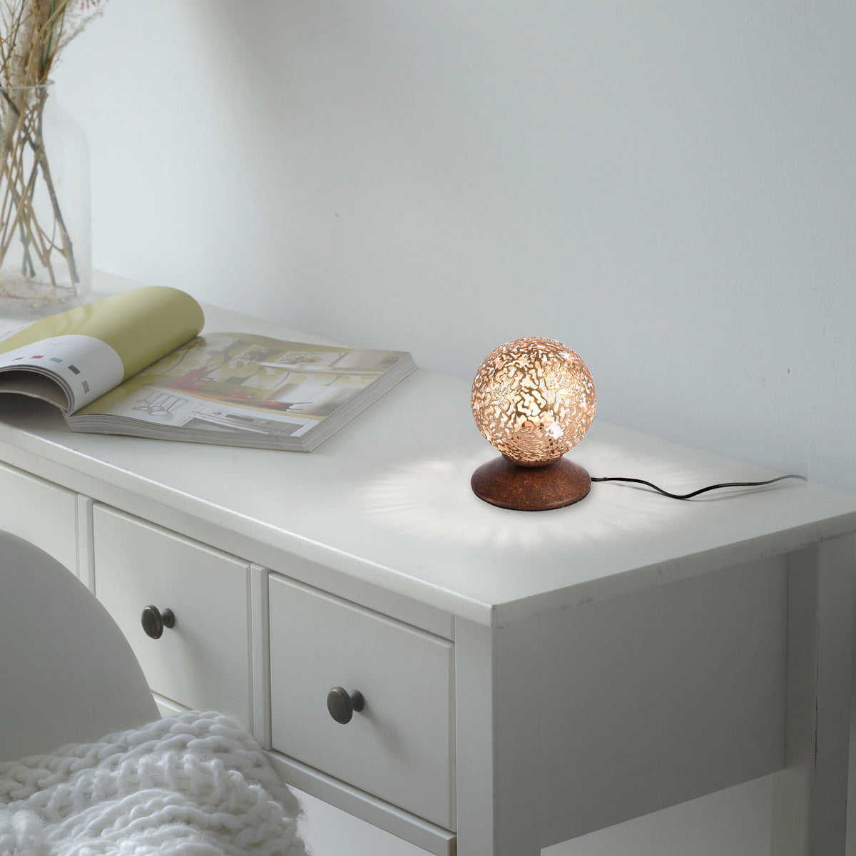 Mise en ambiance : lampe posée sur une commode blanche près d'une revue ouverte
