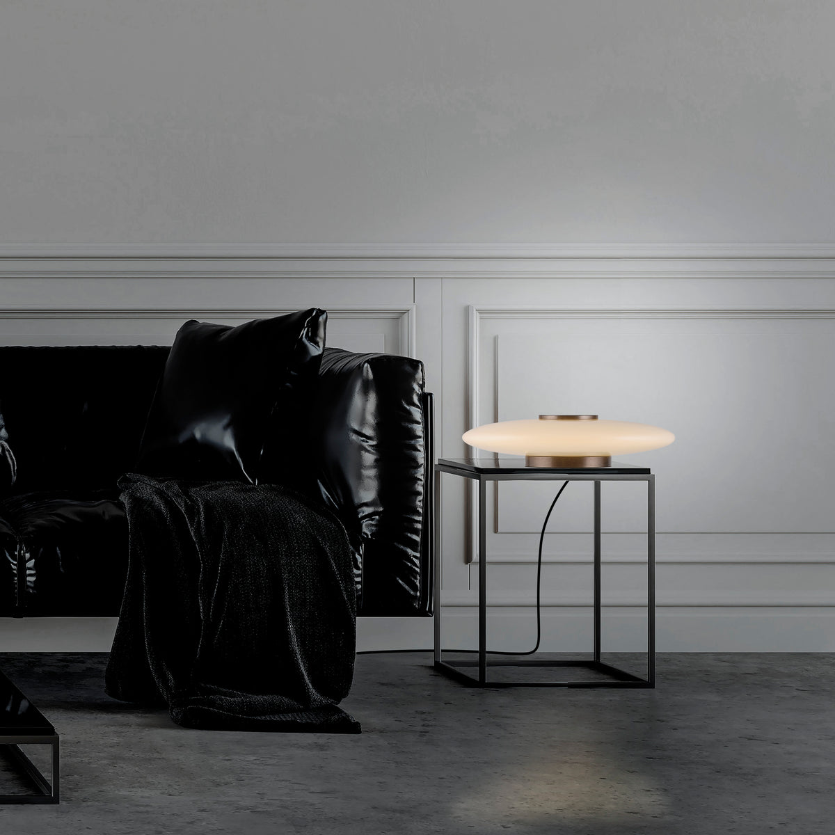 Mise en ambiance dans un salon, lampe posée sur table d'appoint près d'un fauteuil noir.