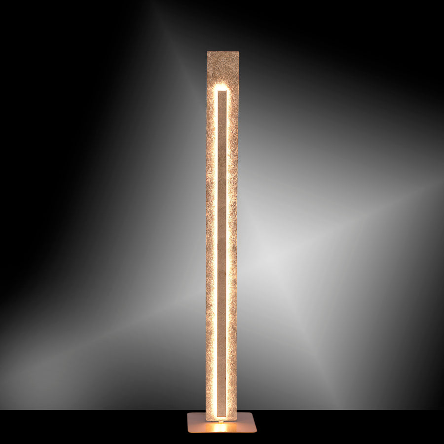 Lampadaire doré allumé dans l'obscurité, halo de lumière chaude projeté au mur.