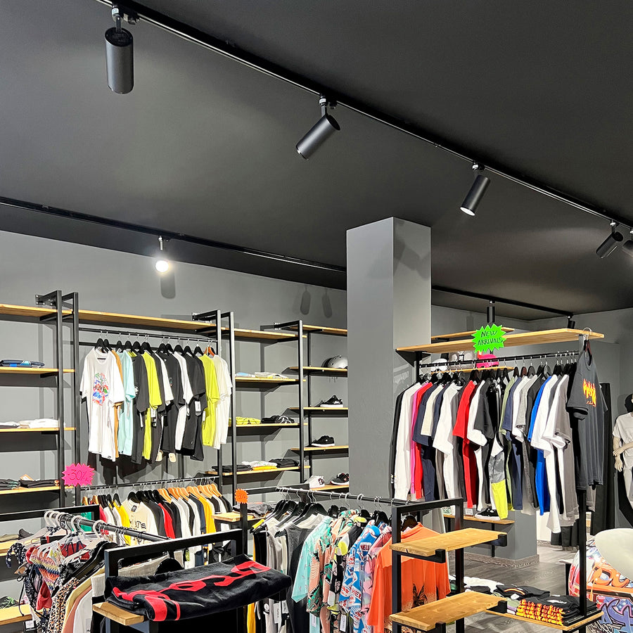 Intérieur de boutique avec plusieurs spots noirs sur rail éclairant les portants de vêtements.