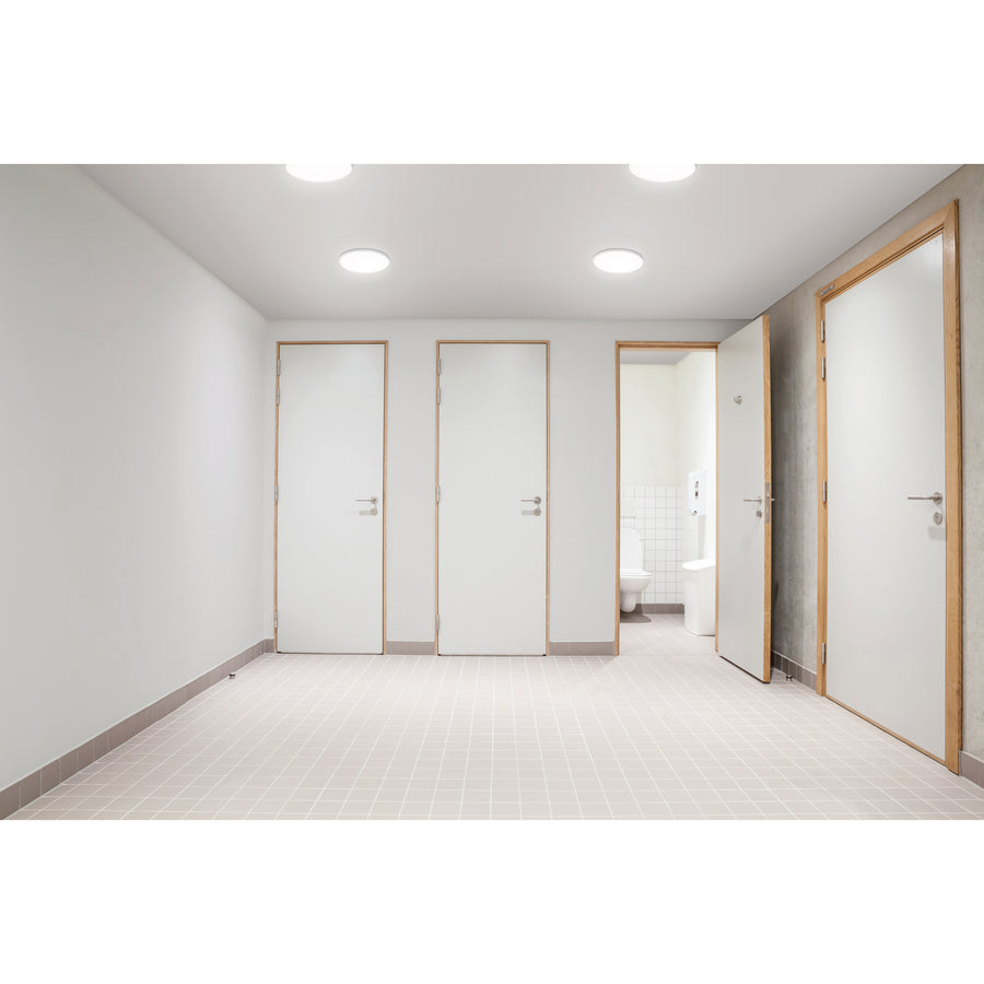Couloir de sanitaires avec plusieurs plafonniers ronds allumés au plafond