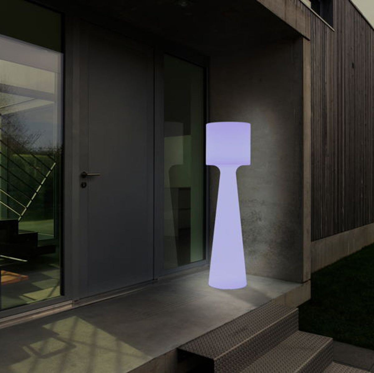 Lampadaire cylindrique éclairé d'une lumière bleutée près d'une porte sombre