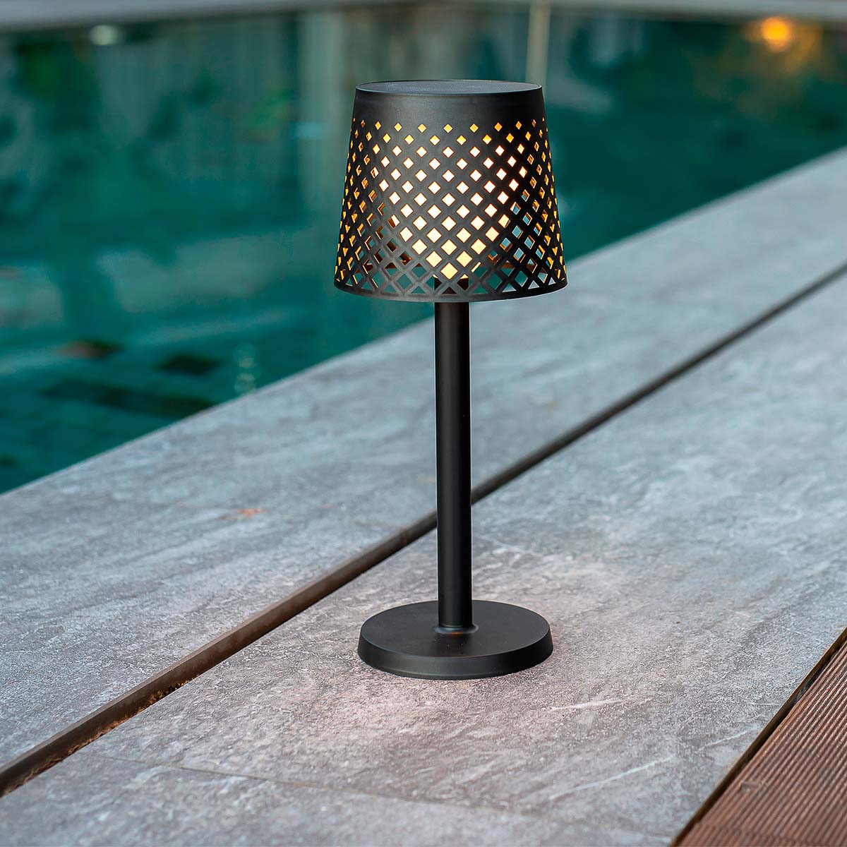 Lampe solaire noire posée sur une table en bois, bord de piscine