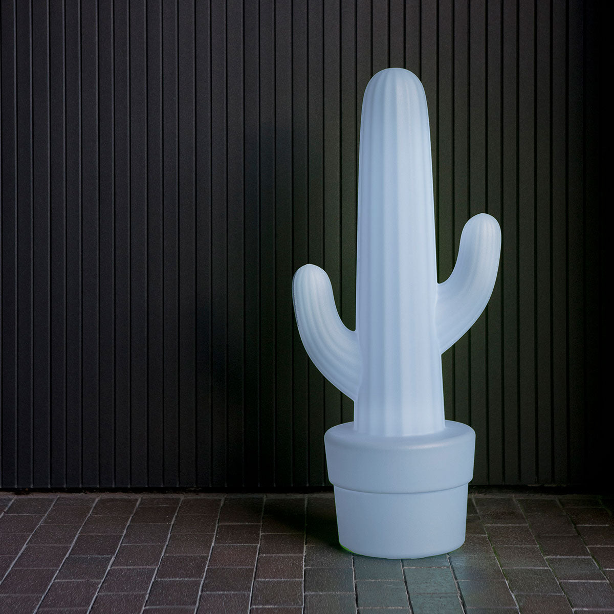Lampadaire cactus blanc éteint devant mur à lattes sombres, sur sol carrelé.